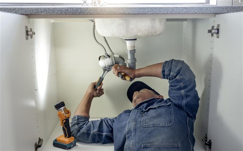 Plumber repairing pipes beneath a bathroom sink in South Pasadena